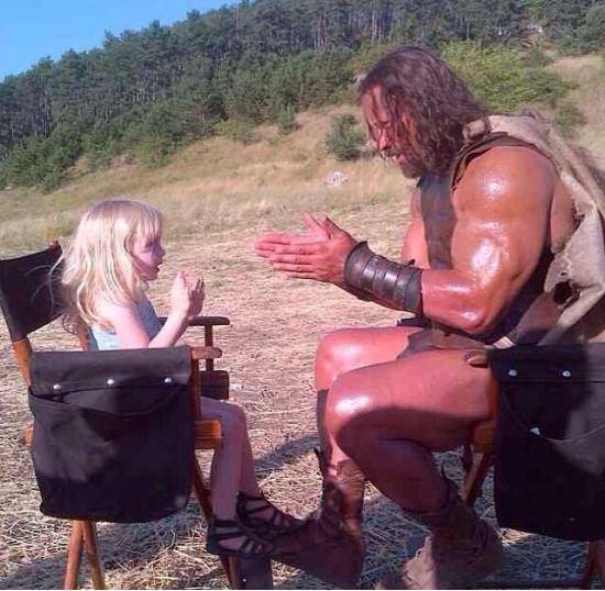 The Rock on set and in costume as Hercules playing party cake with a 3 year old