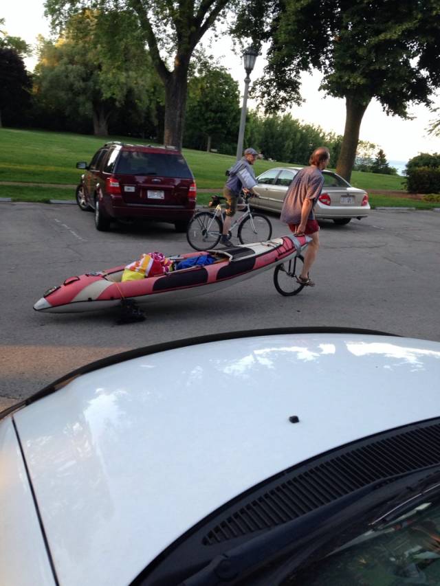 Man on a unicycle pulling a kayak on rollerblades