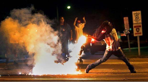 Guy throws a can of tear gas BACK at the cops, without putting down his bag of chips... This is America. It’s not a protest without snacks.
