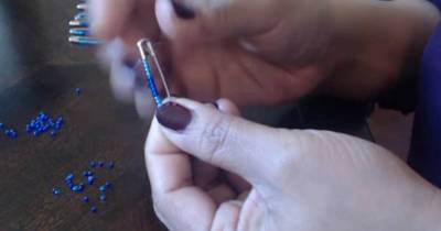 The Woman Puts 12 Beads On A Safety Pin And Places It Down In Front Of Her. Then She Fastens It With An Elastic Band.